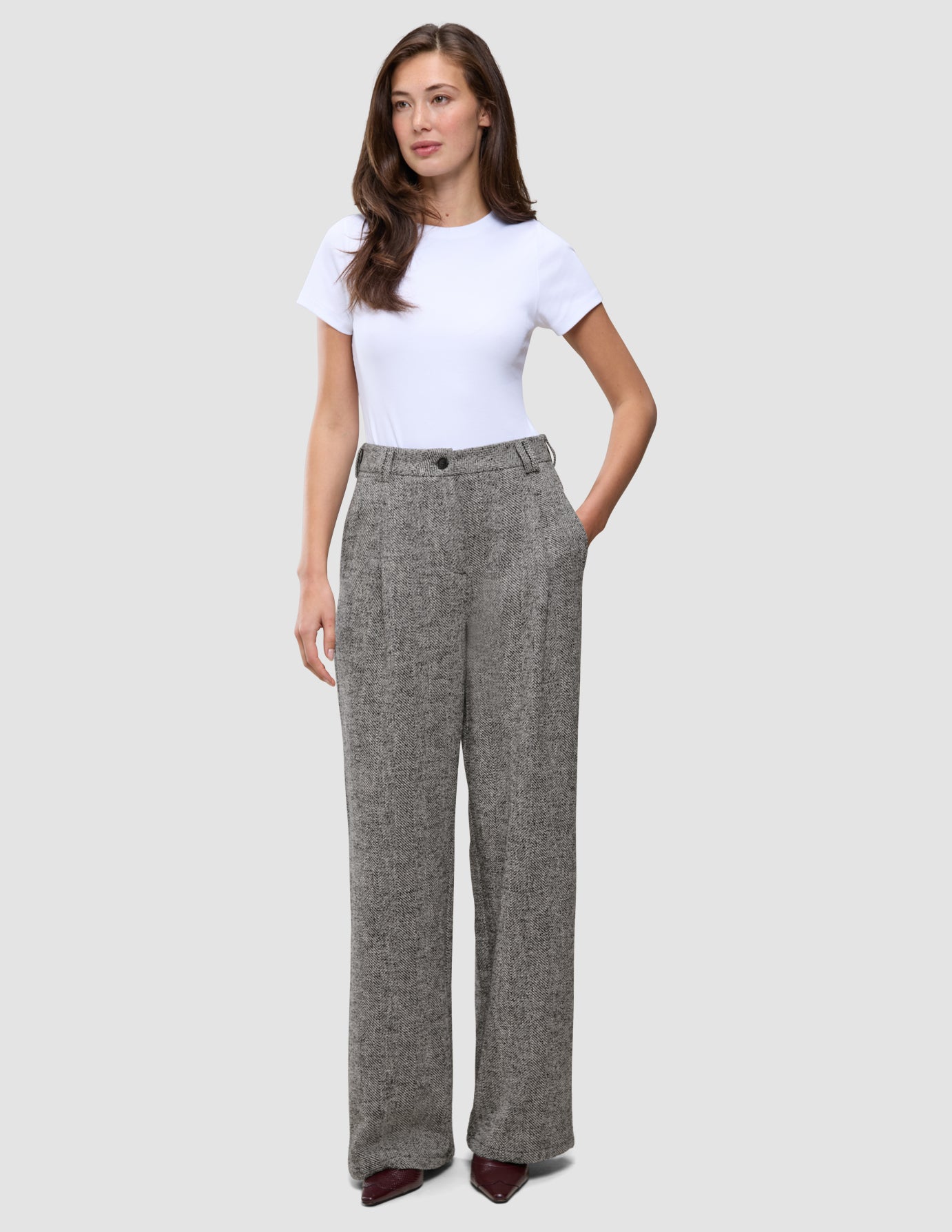 Damenhose Ashryn Wide Domino Herringbone: eine hoch taillierte Hose mit weitem Bein aus grauem Bouclé-Stoff mit Fischgrätenmuster, kombiniert mit einem weißen T-Shirt.